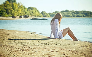 woman wearing white dress shirt sitting on brown sand