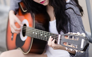 woman wearing gray open cardigan playing brown classical guitar