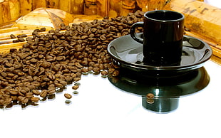 black ceramic mug on saucer surrounded of coffee beans