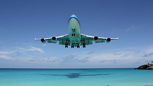 blue and white airplane flying under blue body of water with blue sky backgroudn