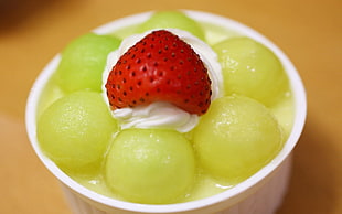 strawberry on top of whip cream and green fruits in white cup
