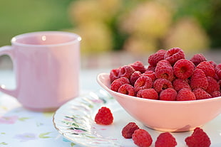 selective focus photography of red raspberries in white ceramic bowl