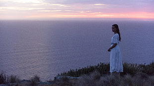 woman wearing white dress standing near ocean