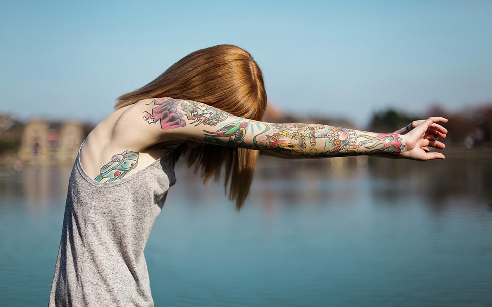 selective photography of woman in gray tank top with arm tattoo near body of water HD wallpaper