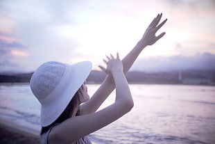 woman in white hat raising hands in front of beach