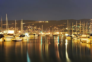 lighted yachts on calm body of water in distance lighted mountain mirrored on water during night time