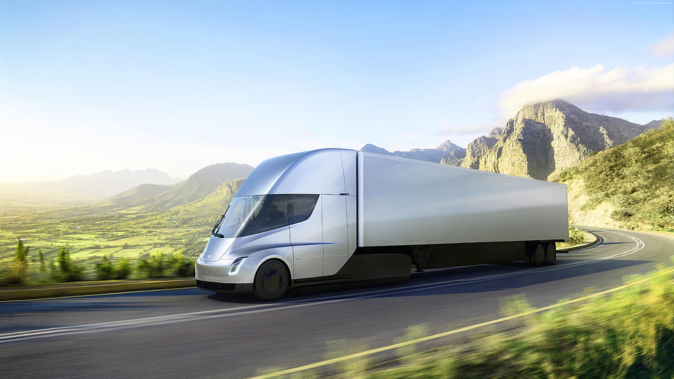 time lapse photography of silver freight truck concept running on curvy road surrounded by green mountains during daytime HD wallpaper