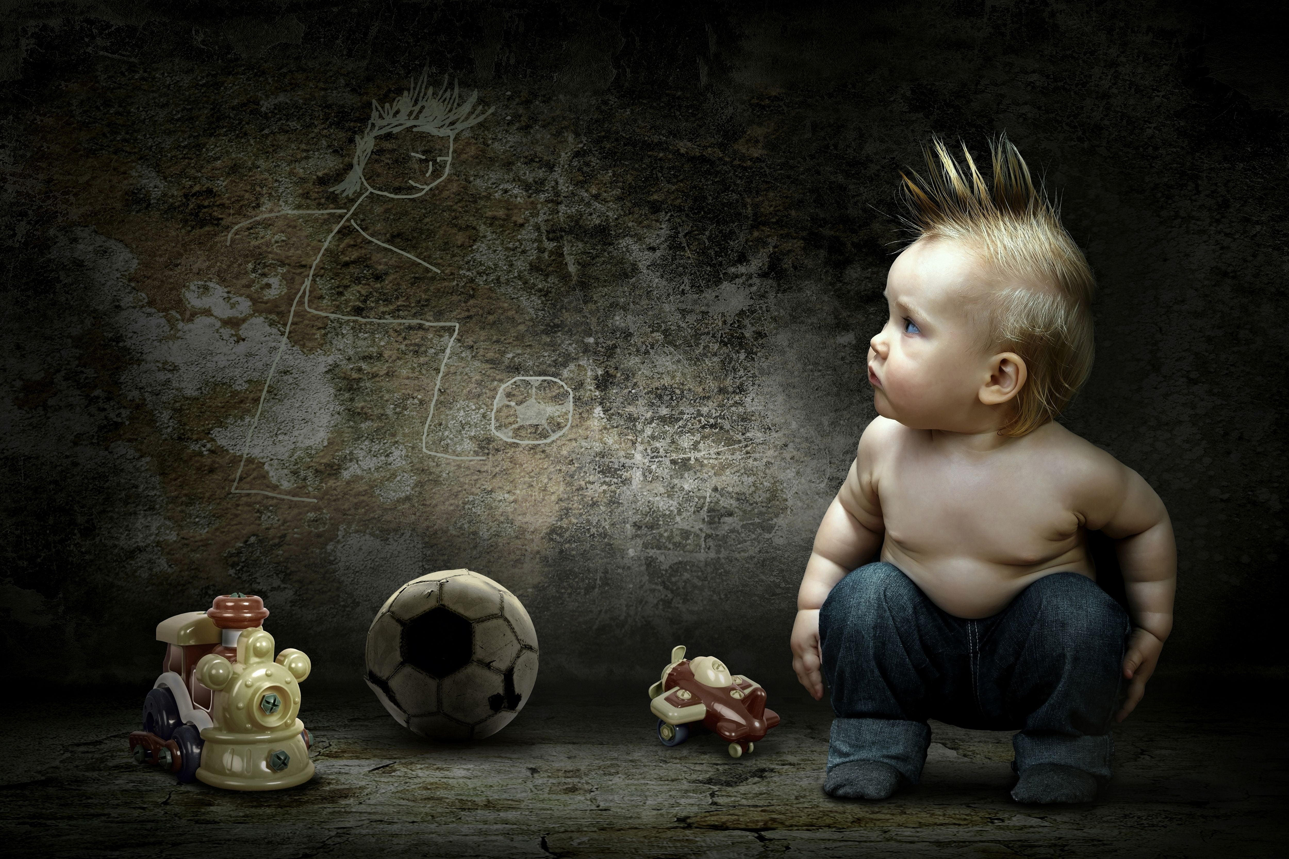 photography of boy with blue jeans sitting near white and black soccer ball