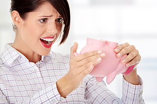 woman in white dress shirt holding pink pig coin bank closeup photo