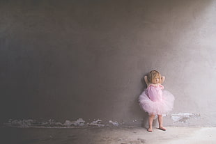 girl wearing pink dress leaning on wall during daytime