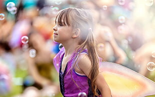 female child wearing purple tank top and flying bubbles