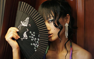 woman holding fan covering nose
