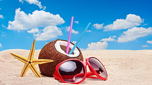 sunglasses, coconut juice and yellow starfish on beach sand