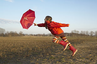 girl in red jacket holding red umbrella on running on green grass field HD wallpaper