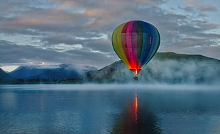 stock photography of multicolored hot air balloon over body of water under cloudy sky, lake hayes