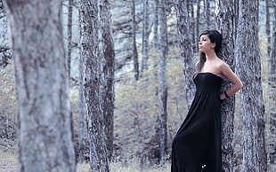 woman wearing strapless long dress leaning on tree trunk in woods
