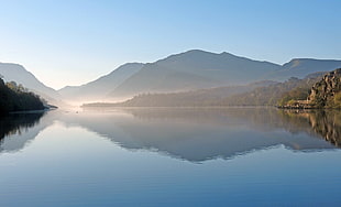 body of water surrounded by mountains with fog under clear sky