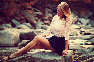 woman wearing white lace crew-neck top and black skirt sitting on rock