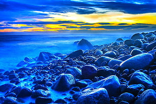 blue stones near body of water at sunset