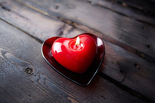 red heart candle on saucer on top of wooden plank