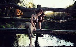 woman in black and red floral monokini sitting on brown wooden bridge over body of water