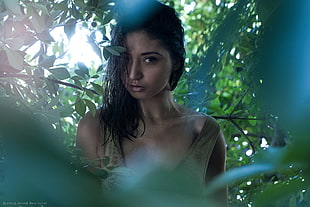 woman wearing tan tank top surrounded by green leaves