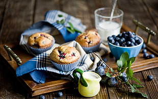 three baked cupcakes on wooden tray with blue berries