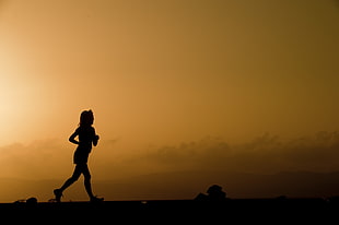 silhouette of a woman running on field under yellow sky HD wallpaper