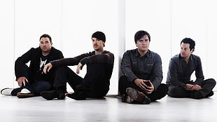 four men wearing black long-sleeved tops sitting on white floor