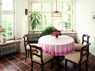 pink roses in white vase on round table with pink cloth inside a white room