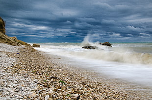 beach with stony sand and wavy waters during daytime