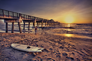 photography of white surfboard on seashore near dock during golden hour