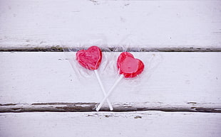 two heart-shaped lollipops on white wood surface