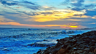 grey rock formation near water with sunset background
