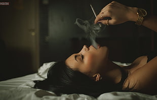 woman lying on bed holding cigarette