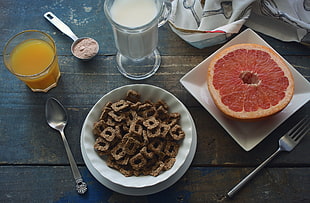 chocolate cereals in white bowl beside sliced fruit in square white saucer