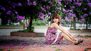 woman wearing floral dress sitting near tree during daytime