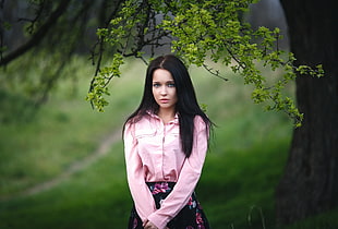 woman in pink dress shirt and black and pink floral skirt standing below tree branch