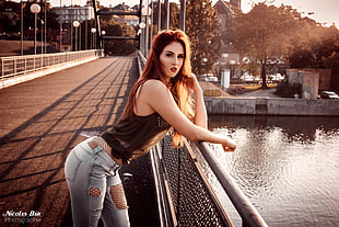 woman in black tank top and distressed grey denim jeans outfit leaning on grey metal fence on bridge during daytime