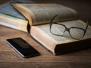 black-framed sunglasses above thick book near Space gray iPhone 6