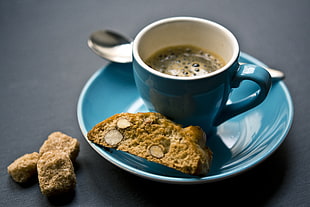 brown sliced bread,blue ceramic mug with coffee inside and stainless steel spoon on top of bowl