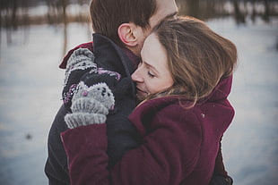 man wearing black snow jacket hugging woman wearing maroon snow jacket