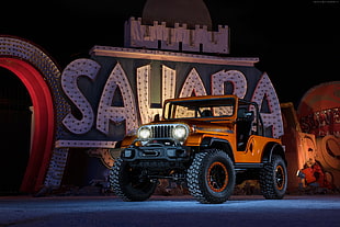 orange Jeep Wrangler parked beside white and black Sahara wall