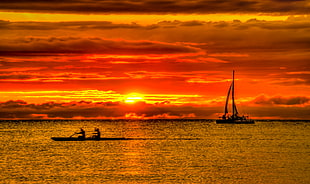 two persons on boat rowing near sailboat during golden hour