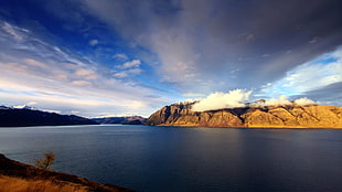 calm body of water beside brown mountain under blue sky