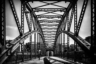 grayscale photography of person walking on steel bridge