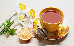 beige ceramic teacup with beverage near sliced orange fruit