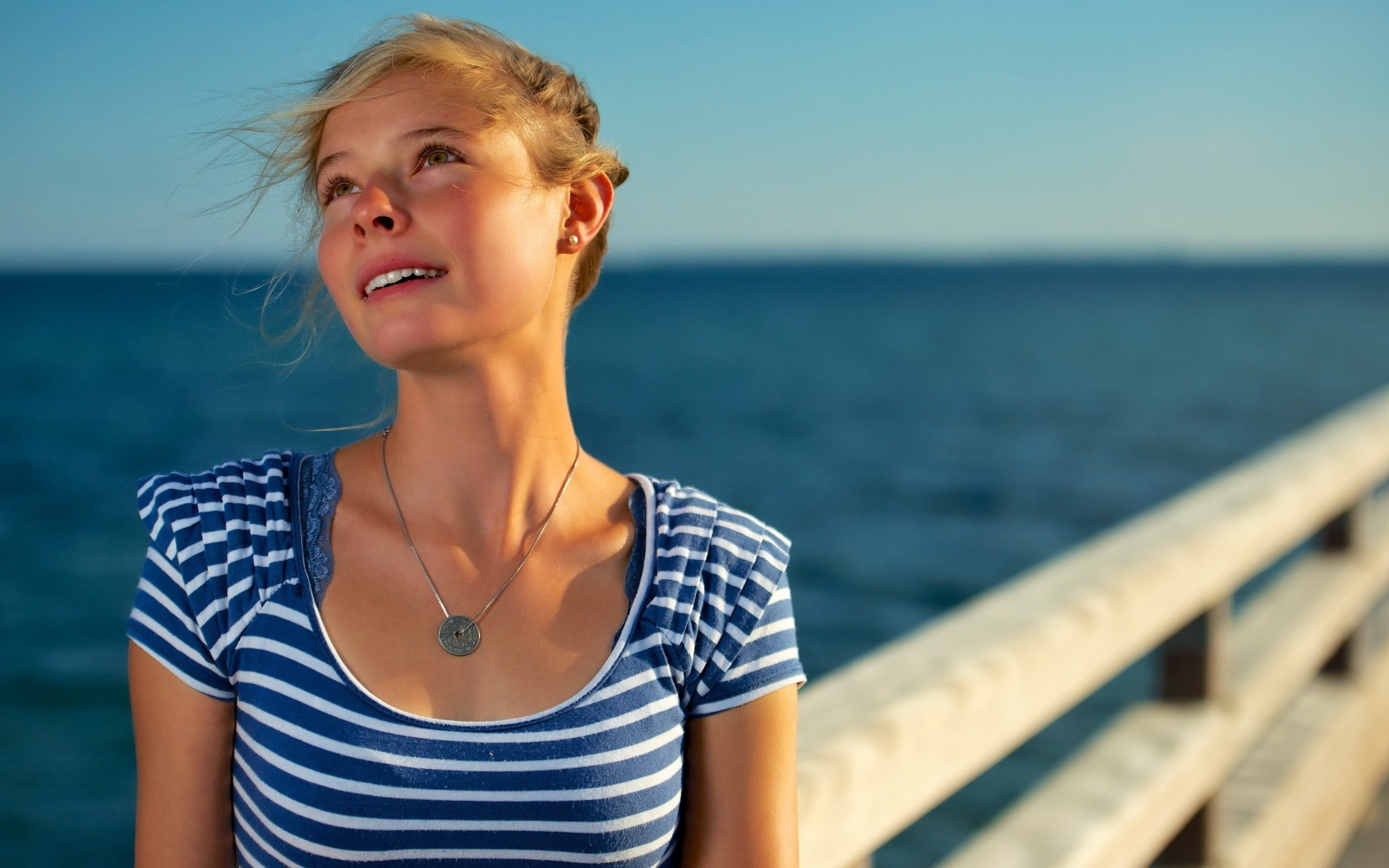 shallow focus photography of a woman in white and blue striped scoop neck blouse on docking pier