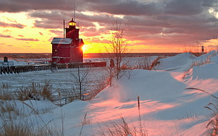 photography of red lighthouse on snowy land during sunset