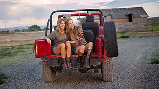 two women riding on the back of red Jeep Wrangler